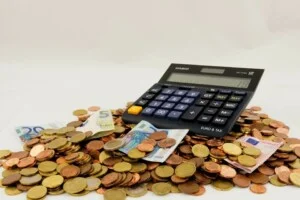 Uma calculadora exibindo números fica em uma grande pilha de moedas misturadas, incluindo moedas e notas de euro, simbolizando o complexo processo de pagamentos de IVA no Chile.