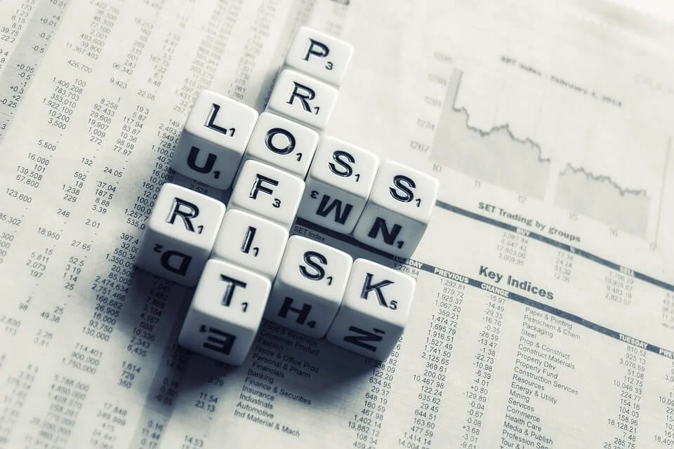 Scrabble tiles spelling out "PROFIT," "LOSS," "RISK," and "FUND" are arranged on a financial newspaper displaying stock market charts and data, providing a snapshot of the intricacies involved in formação da empresa.