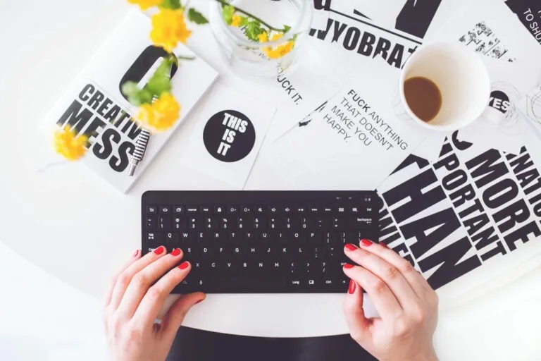 Pessoa digitando em um teclado ao lado de folhetos