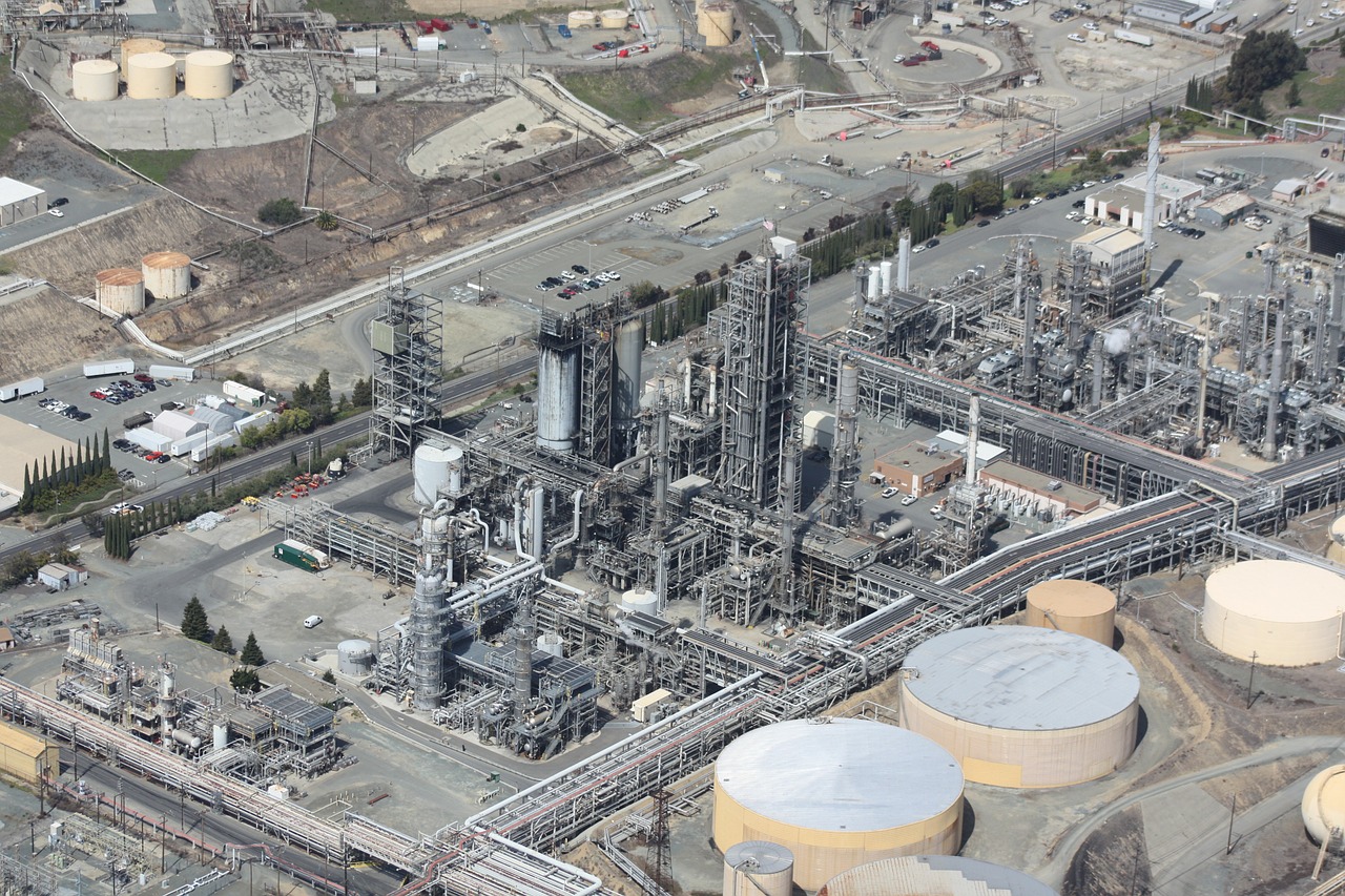 Vista aérea de um complexo de refinaria industrial com várias tubulações, tanques de armazenamento e estruturas. A instalação se estende por uma grande área com vários edifícios, contêineres e maquinário. O terreno ao redor inclui alguma vegetação e outras instalações industriais. A devida diligência na Bolívia garante a conformidade e a eficiência do local.   