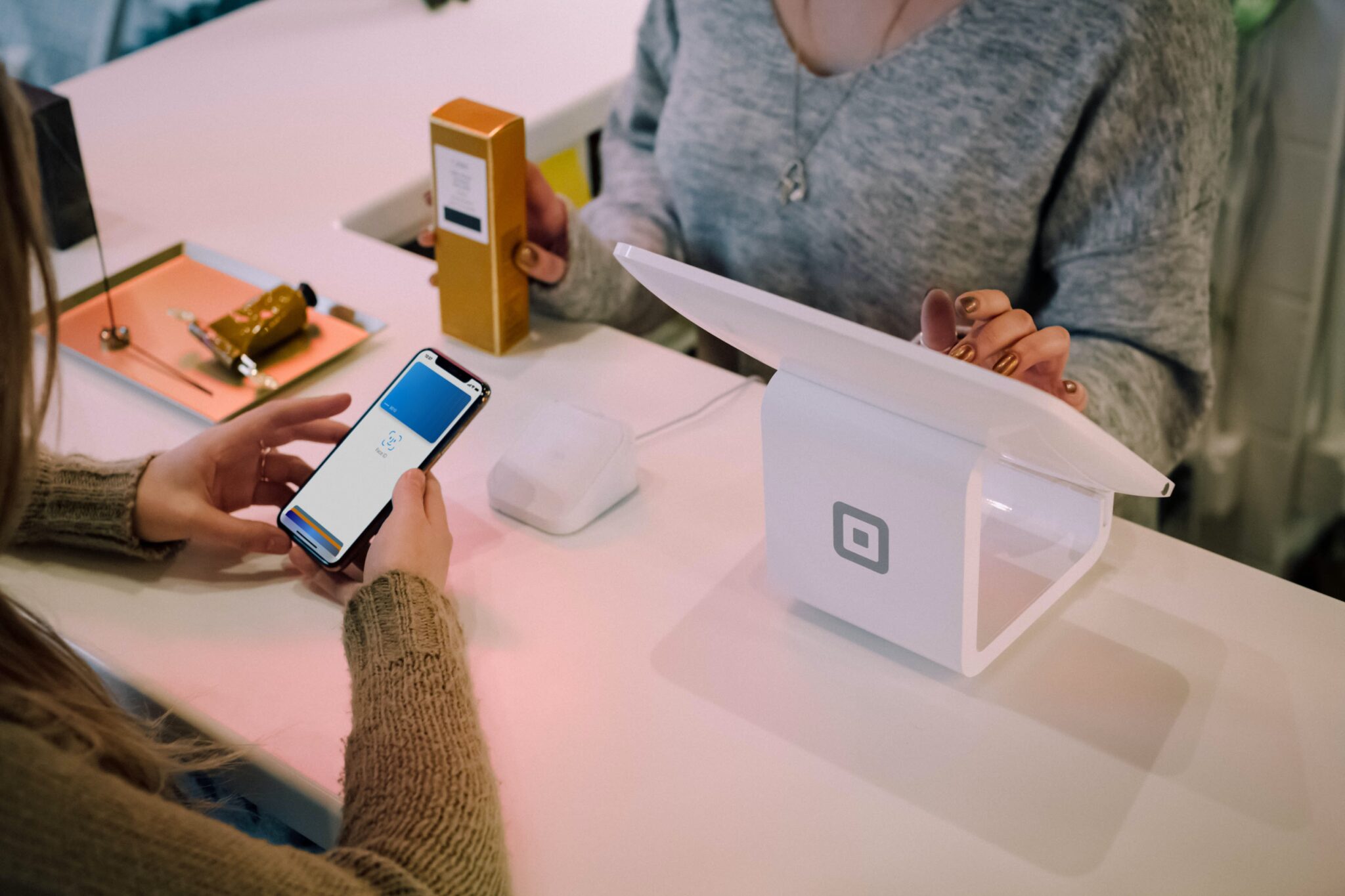 Duas pessoas estão em um caixa de supermercado. A pessoa à esquerda está segurando um smartphone, exibindo uma tela de pagamento. A pessoa à direita está verificando a transação em um tablet conectado a um leitor de cartão Square branco, mostrando os avanços no setor financeiro da Austrália.  