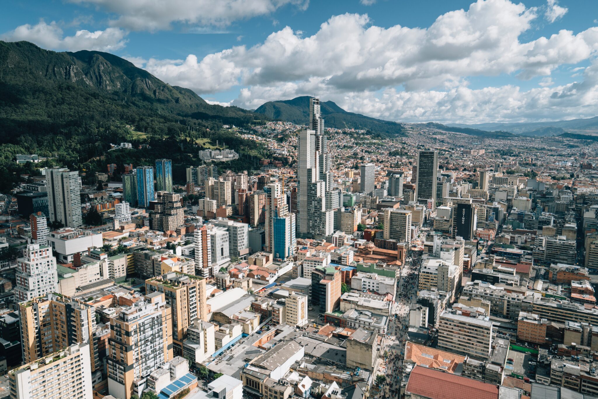 Vista aérea de uma grande cidade na Colômbia com uma mistura de prédios modernos e estruturas baixas, cercada por montanhas sob um céu parcialmente nublado. A linha do horizonte reflete as complexidades relacionadas à realização de um estudo de preço de transferência em uma região economicamente tão diversa. 