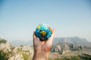 Una mano sosteniendo un pequeño globo terráqueo con vistas a las montañas y un cielo azul de fondo, enfatizando regiones como África y América. Esta representación visual subraya sutilmente conceptos globales, incluidos los impuestos internacionales.