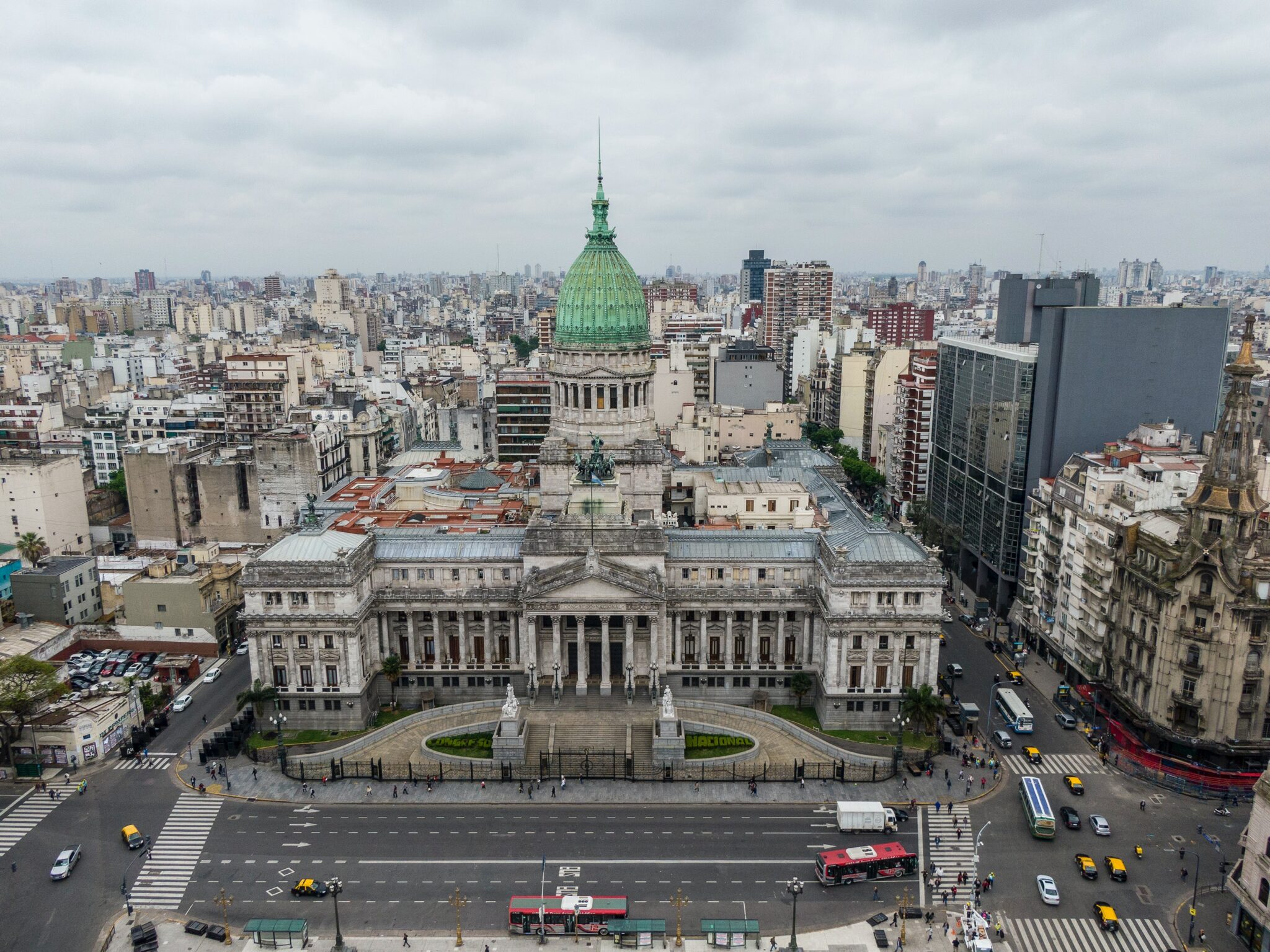 Aerial view of the Argentine National Congress building in Buenos Aires, Argentina. The structure features a green dome and neoclassical architectural design. It is surrounded by city buildings and a busy street with traffic and pedestrians, emblematic scenes often highlighted by a local director in Argentina.