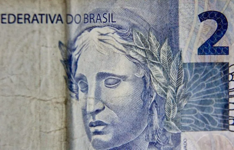 Imagen en primer plano de un billete de 2 reales brasileños. El lado izquierdo muestra parte del texto "FEDERATIVA DO BRASIL" y presenta el grabado de un rostro coronado, probablemente una figura simbólica, con hojas detalladas en la corona, un recordatorio del intrincado panorama financiero que incluye los precios de transferencia en Brasil.