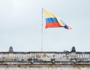 Una bandera de rayas amarillas, azules y rojas con un escudo de armas ondea sobre un edificio de piedra con tallas ornamentadas en el techo, contra un cielo nublado, simbolizando la profundidad histórica entrelazada con las obligaciones tributarias modernas en el Perú.