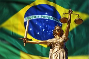 A bronze statue of Lady Justice holding scales in her left hand and a sword in her right stands resolutely in front of a large Brazilian flag with the slogan "Ordem e Progresso." This powerful image underscores the importance of Direito do Trabalho no Brasil.