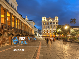 Una calle de una ciudad de Ecuador se ve al atardecer, con un edificio iluminado adornado con columnas a la izquierda y un edificio decorativo iluminado a lo lejos. La gente camina por el sendero empedrado. El logotipo de Biz Latin Hub y el texto "Hacer negocios en Ecuador" se superponen a la imagen.