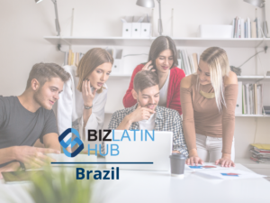 Cinco personas están reunidas alrededor de una computadora portátil en una oficina, colaborando en un proyecto. Al fondo se ven estantes con archivos y material de oficina. El texto "BIZ LATIN HUB Brasil" se muestra de manera destacada en primer plano, lo que sugiere que pueden estar consultando con un cazatalentos en Brasil.