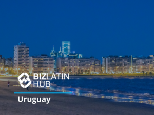 A view of the Montevideo skyline in Uruguay at night, with city lights illuminating the buildings. The photo features a person walking along the sandy shore in the foreground, highlighting Uruguay's reputation as one of the best countries for doing business, with BizLatin Hub branding overlaid on the image.