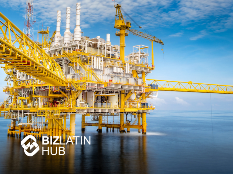 An offshore oil platform with multiple structures and equipment is situated in the middle of the ocean. Yellow steel beams and cranes are prominent, with a clear blue sky and calm sea in the background. The BizLatin Hub logo is in the foreground, highlighting their expertise in nearshoring in the Dominican Republic.