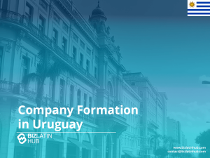 Imagen promocional para Biz Latin Hub sobre la creación de empresas en Uruguay. El fondo muestra una calle urbana con edificios históricos y palmeras, sobrepuesta con un tinte azul. La bandera uruguaya aparece en la esquina superior derecha.